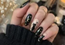 Black cat nails with glossy black polish, cute cat artwork, gold stars, moon details, and elegant Halloween-inspired nail design on real hands.