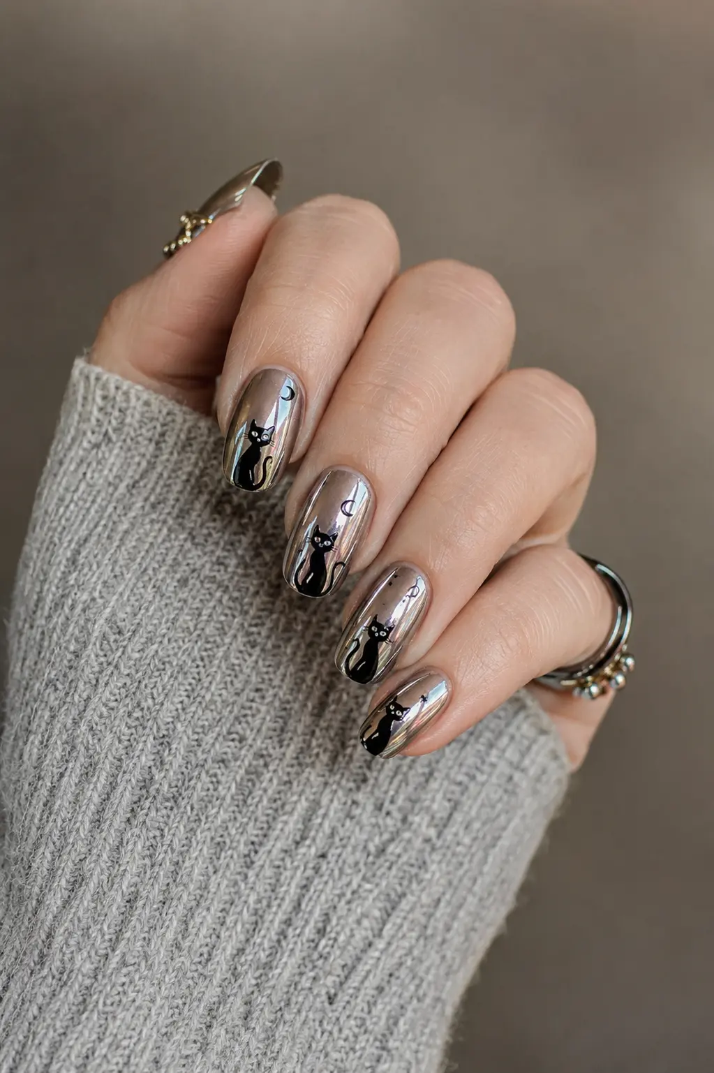 Black cat chrome nails with reflective metallic shine, moon accents, glossy finish, and elegant spooky nail art on a hand with stylish rings.