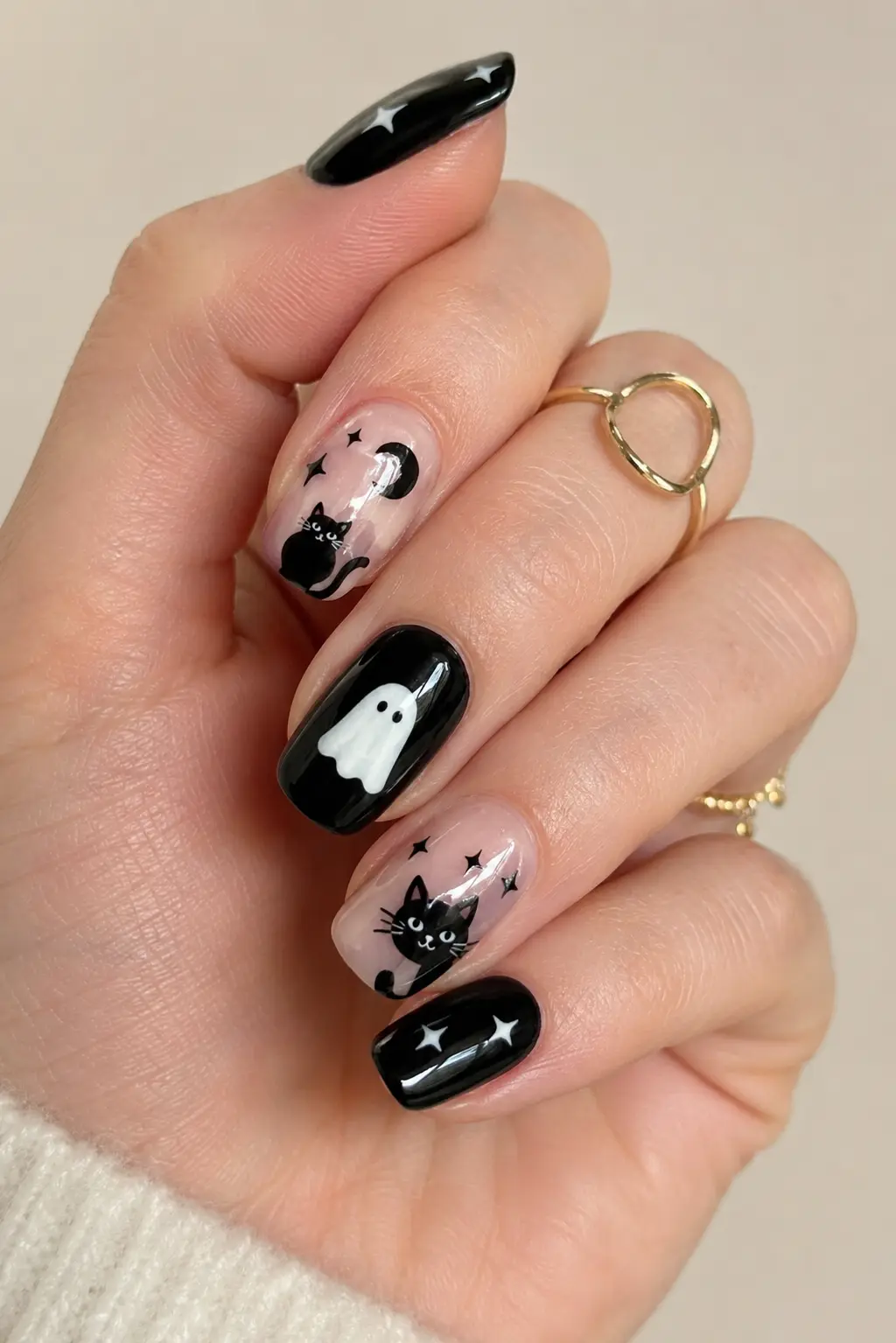Glossy black cat and ghost Halloween nails with cute spooky details, tiny stars, clean manicure finish, and elegant gold rings.
