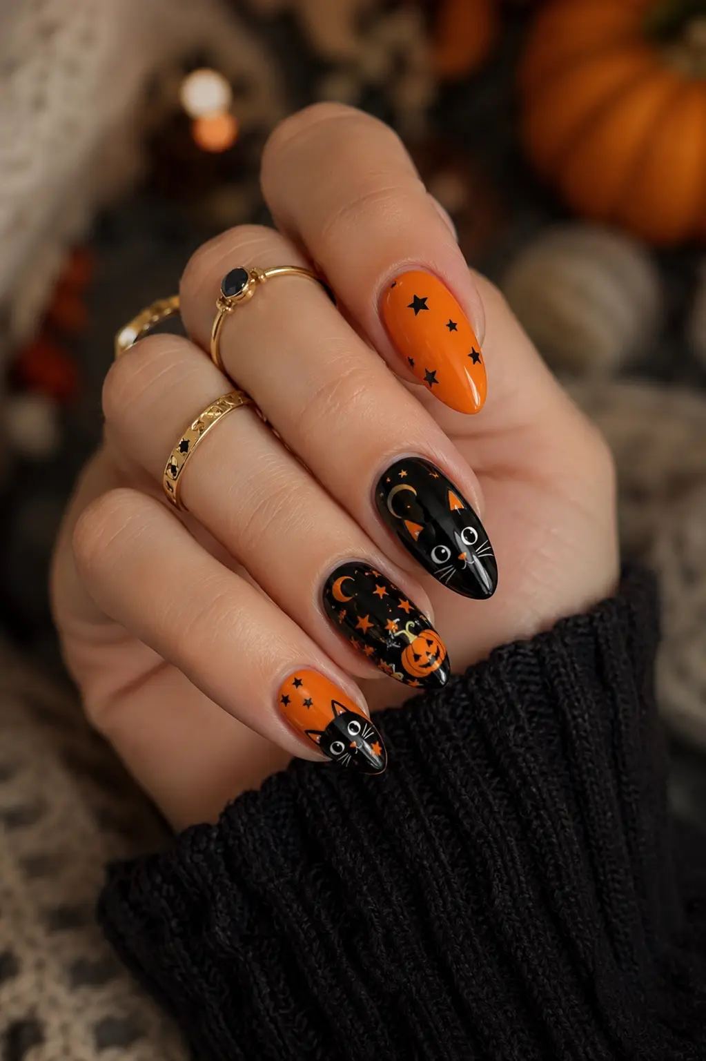 Glossy orange and black Halloween nails with cute black cat art, pumpkin details, tiny stars, gold rings, and a cozy fall background.
