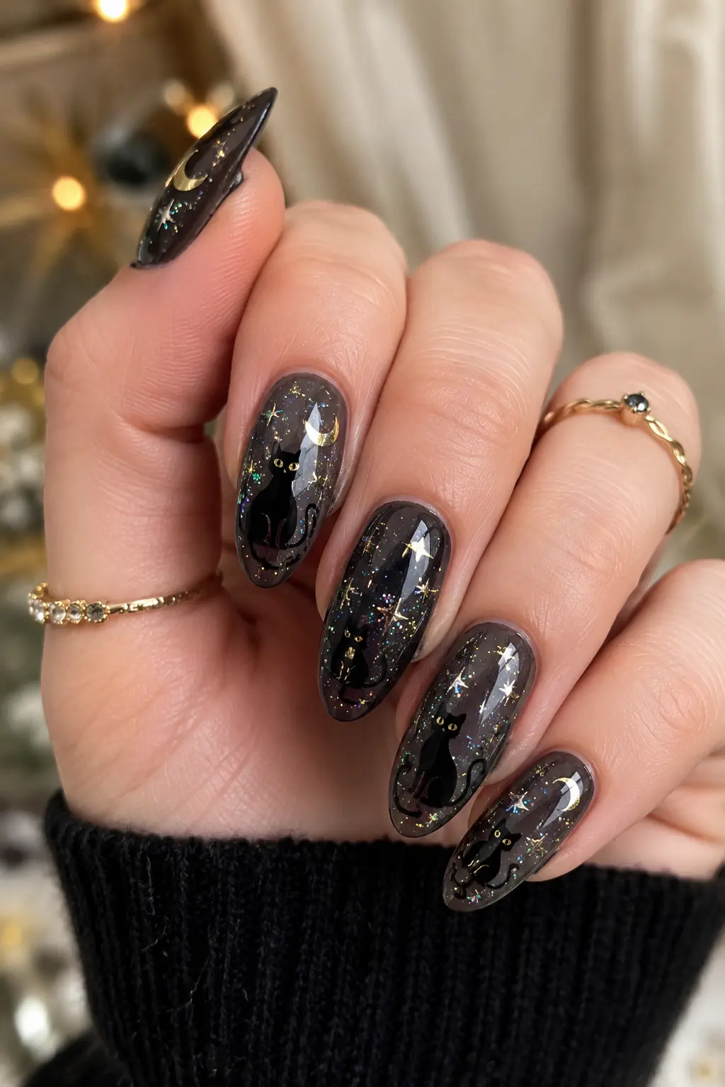 Glossy black cat star nails with glitter, moon details, and night sky artwork on an elegant hand with gold rings.