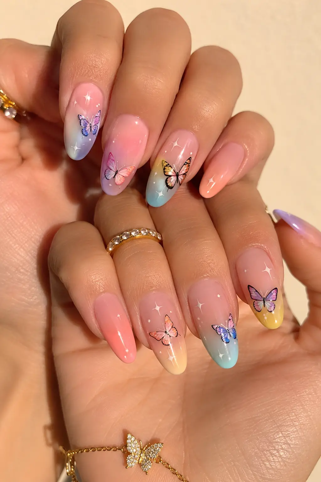Pastel butterfly summer nail design on realistic women’s hands featuring glossy gradient gel nails, tiny butterfly artwork, almond-shaped nails, clean cuticles, gold jewelry, and soft natural lighting.