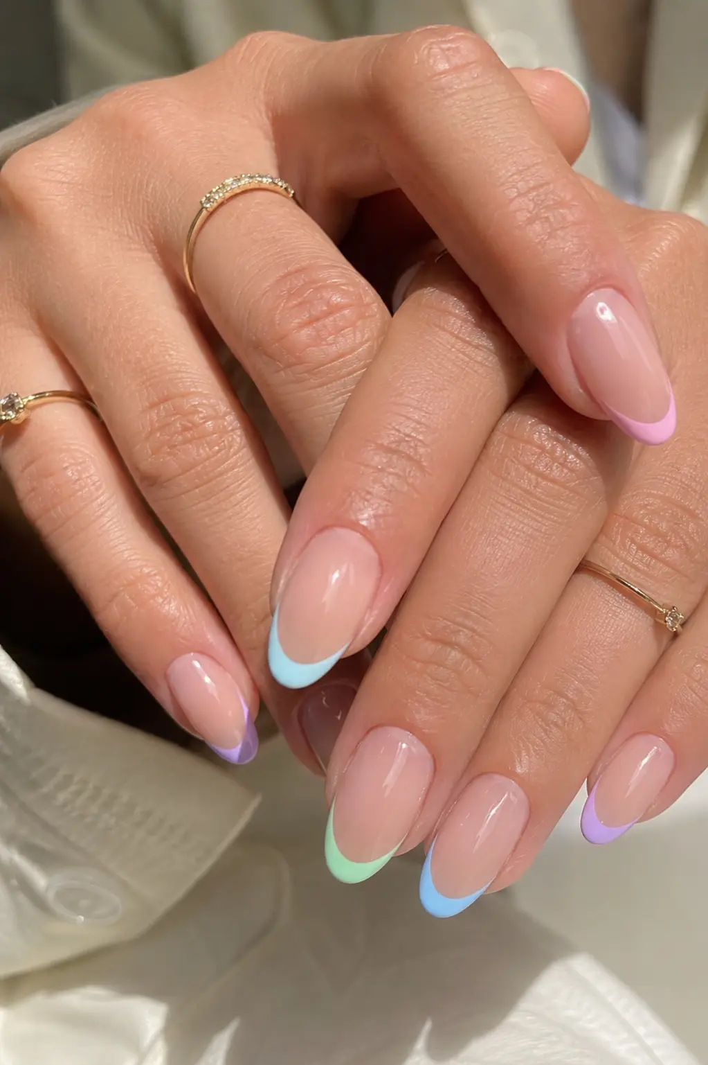 Pastel French tip summer nail designs on real women’s hands featuring glossy nude almond nails with pink, blue, lavender, and mint tips, clean cuticles, delicate gold rings, and soft natural daylight.