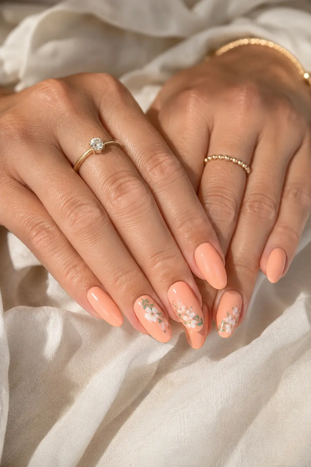 English woman’s hands featuring glossy peach pastel summer nails with delicate floral nail art, almond-shaped gel manicure, gold jewelry, and soft ivory background.