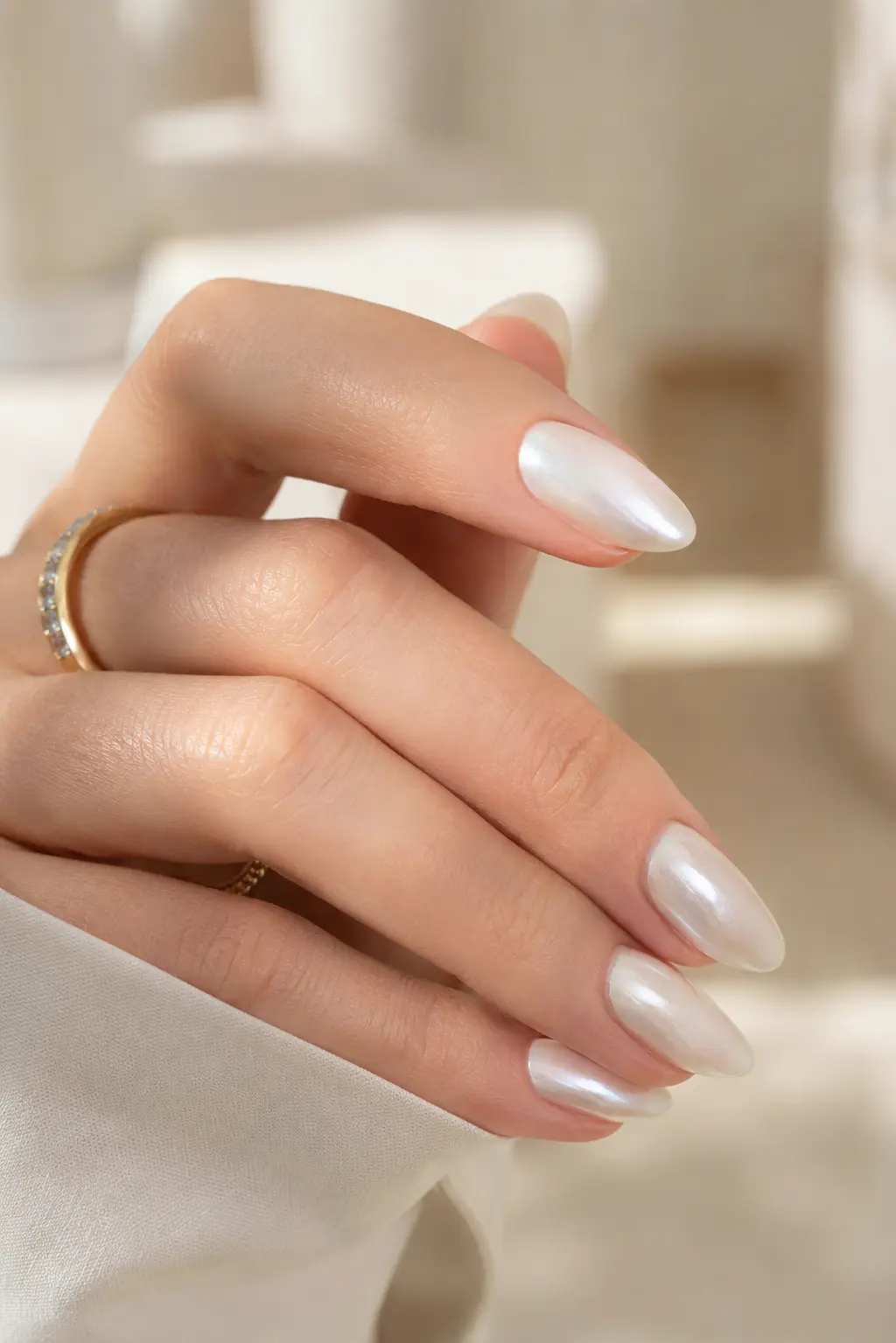 woman's hand with glossy pearl white almond-shaped nails in a close-up DSLR-style photo, featuring a luminous finish, natural skin texture, soft daylight, and a luxurious cream background.