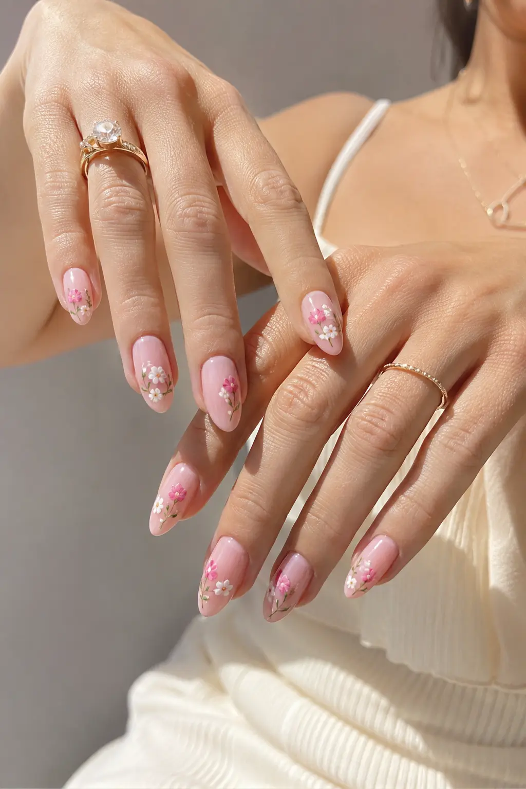 lose-up of real woman’s hands featuring soft pink glossy gel almond nails with delicate floral summer nail art, clean cuticles, feminine rings, and luxury July manicure style in bright natural daylight.